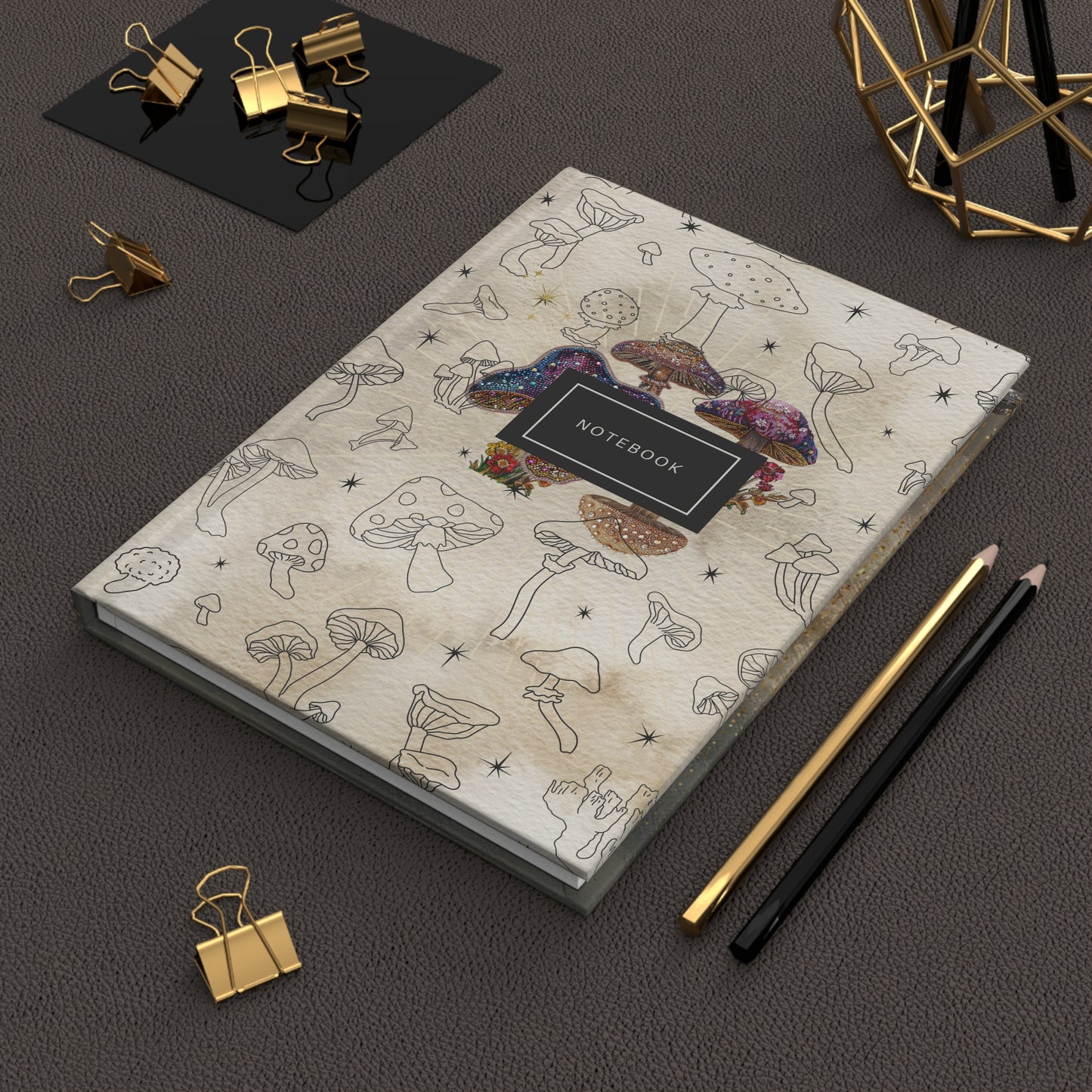 Mystical mushroom notebook with hand-drawn illustrations and sequined accents on top of a desk with pencils and clips
