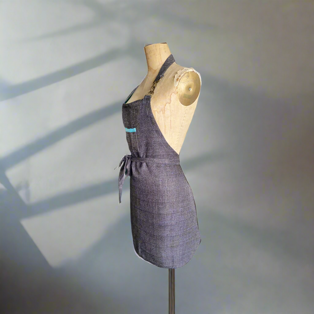 An angled side view of the lux double-sided apron with a front pocket and aqua trim displayed on a mannequin.