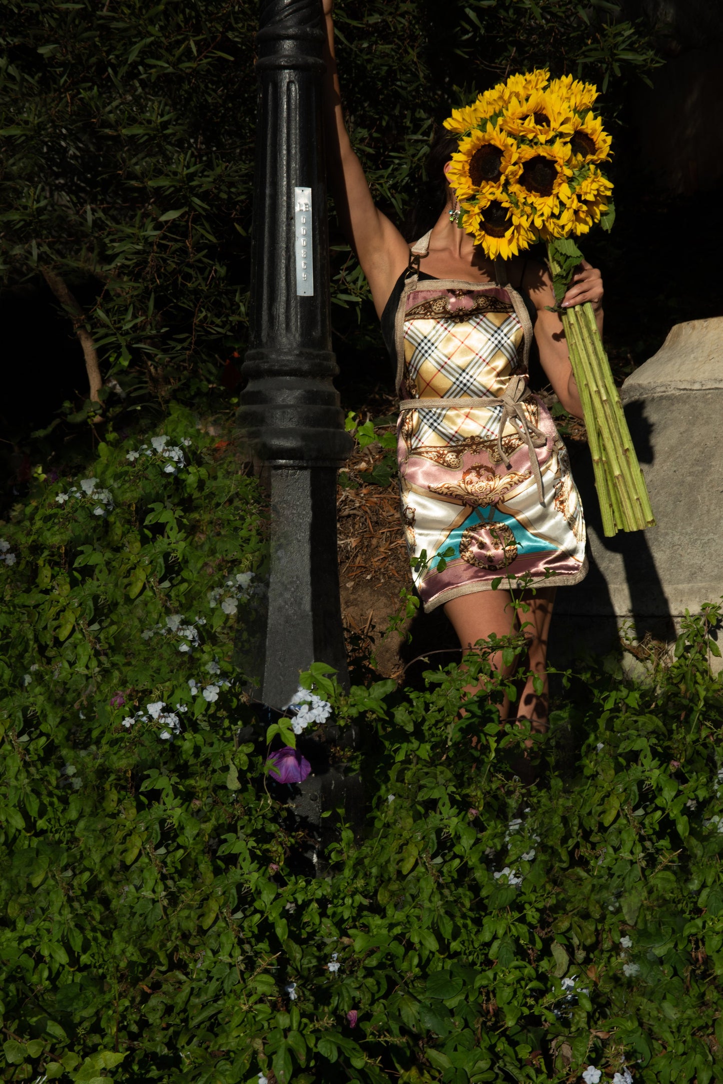 Woman holding sunflowers standing next to a lamppost in a garden setting