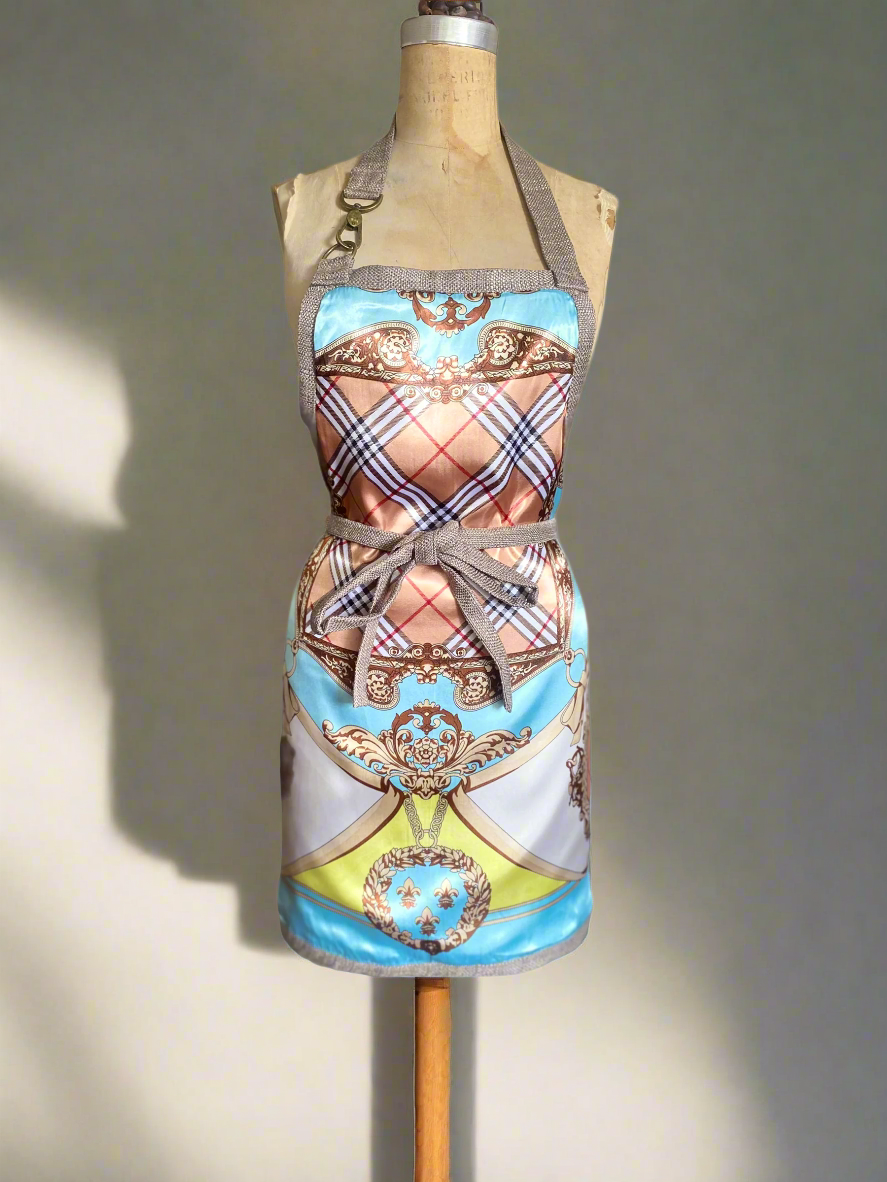 An aqua multicolored, with plaid design, double-sided apron. Includes a snap hook detail displayed on a mannequin.