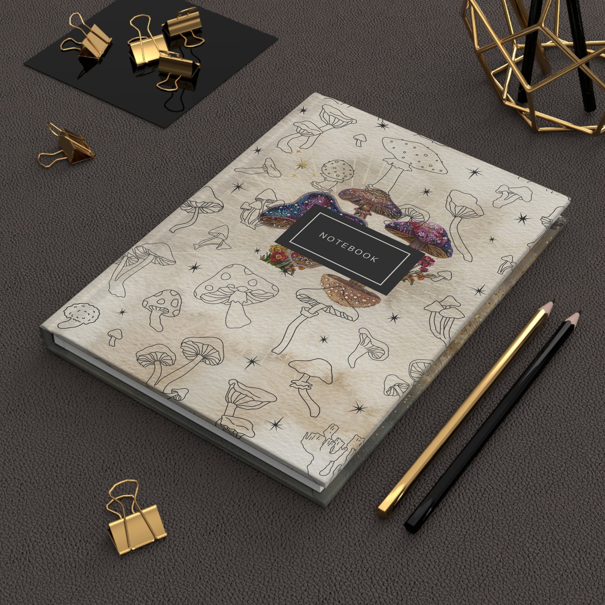 Mystical mushroom notebook with hand-drawn illustrations and sequined accents on top of a desk with pencils and clips