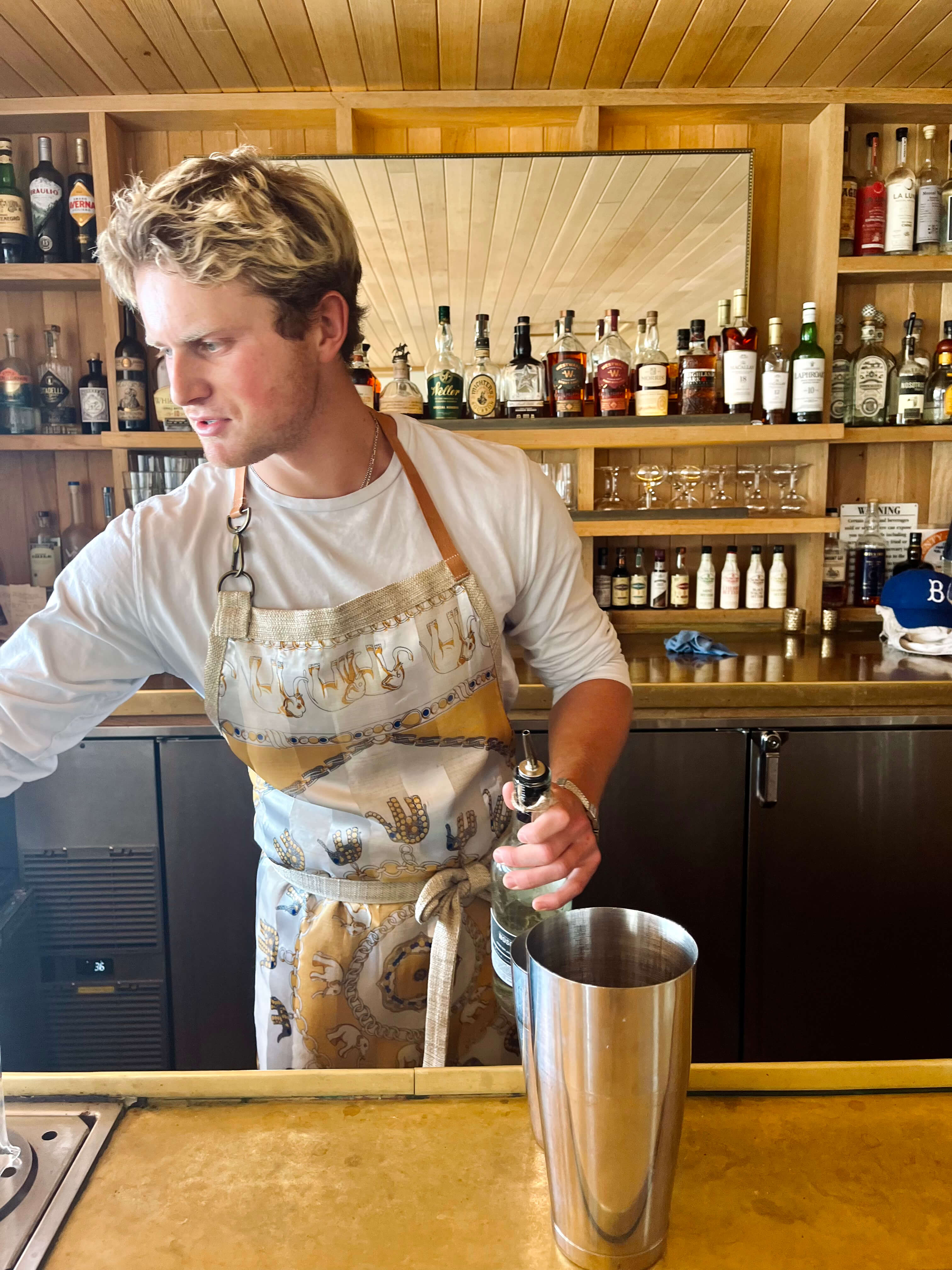Bartender in Reloveler Designs apron preparing cocktail at an elegant bar