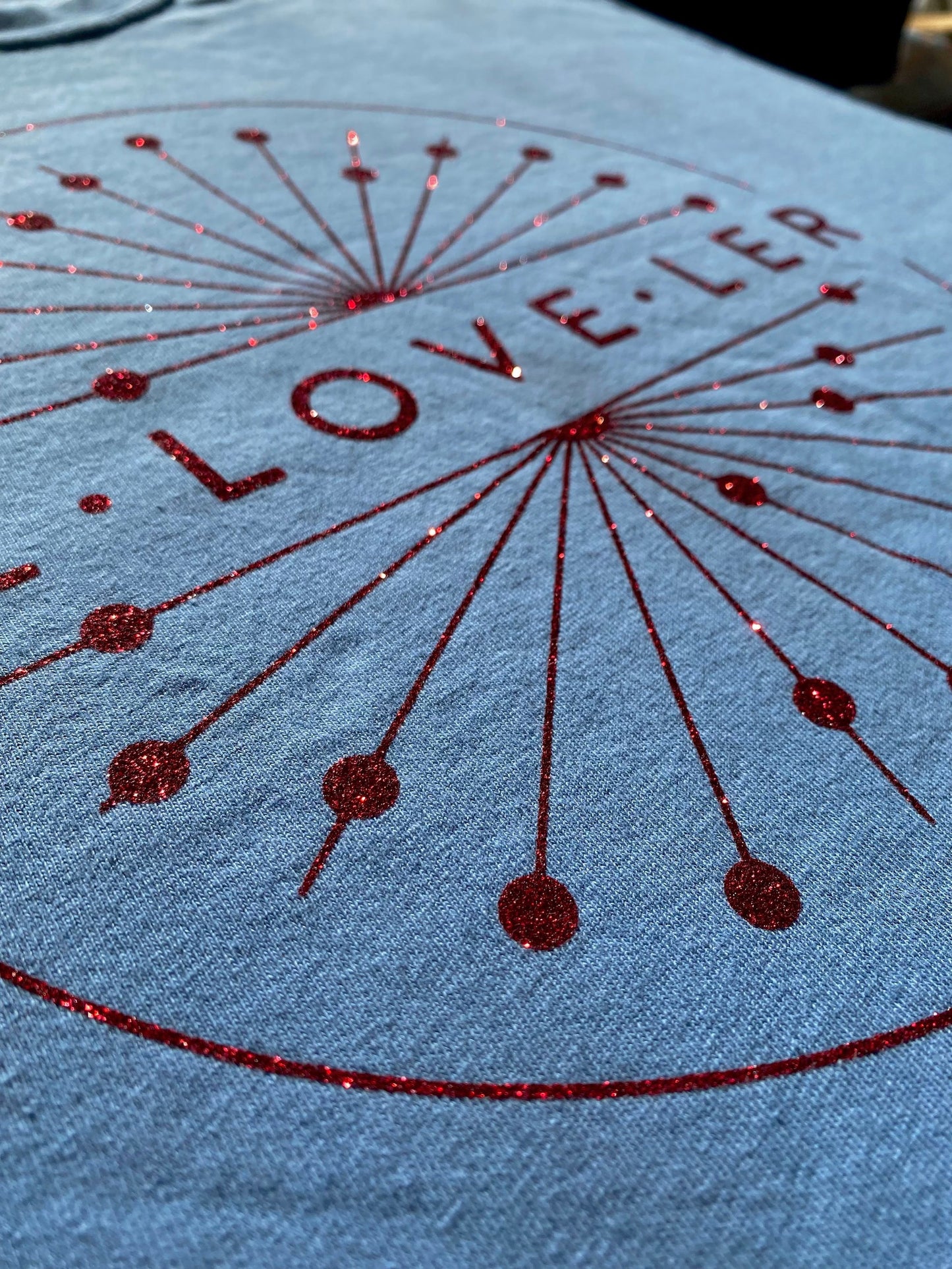 Blue t-shirt close up showing detail of glitter design. 