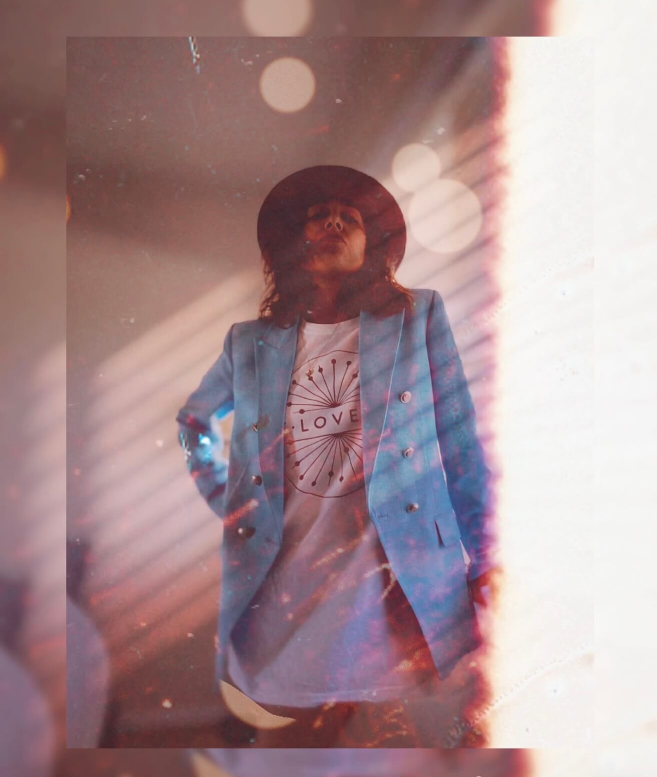 Person wearing LOVE graphic t-shirt with blue blazer and wide-brim hat on a blurred background