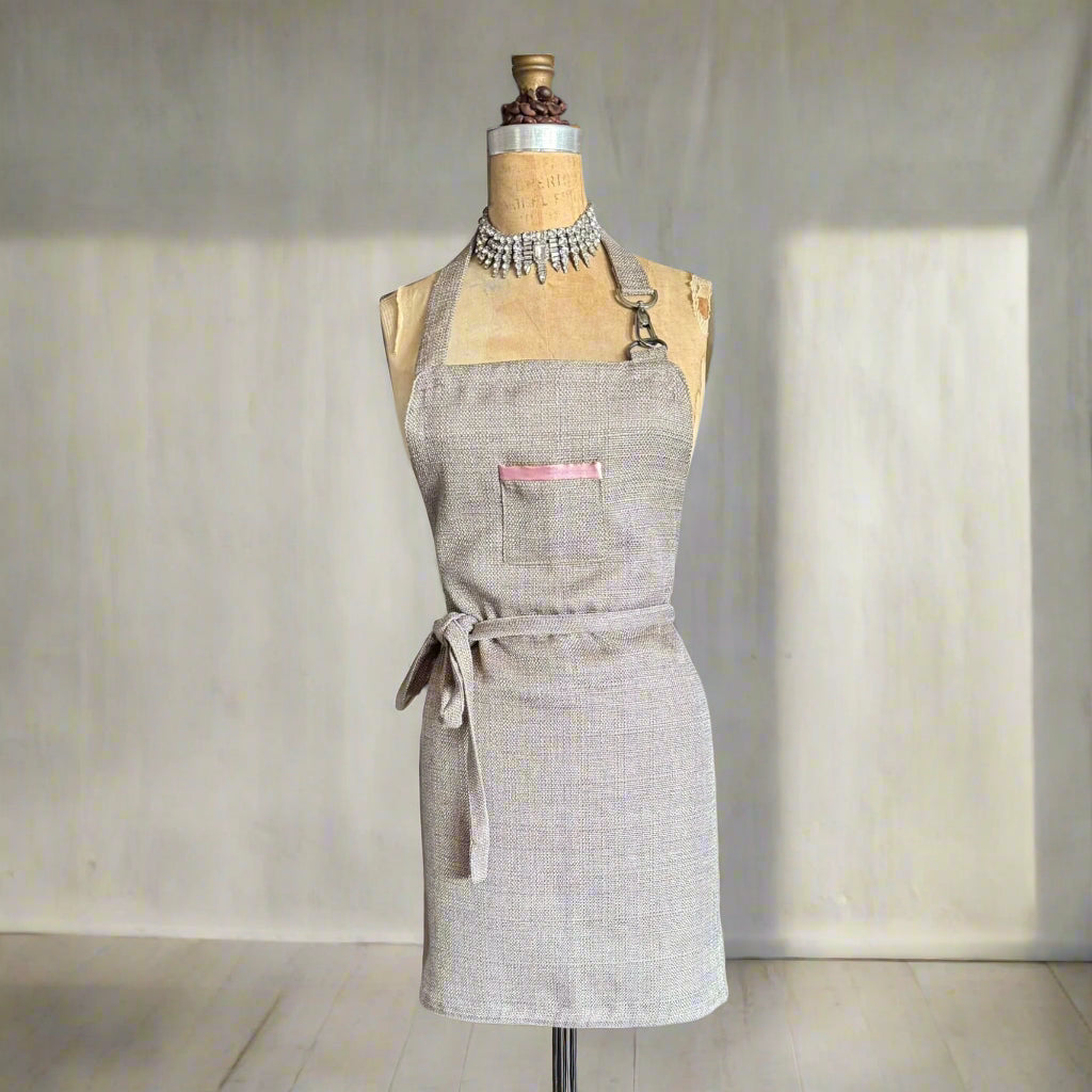 Gray apron on a mannequin showing pink lined detail on pocket against a plain background